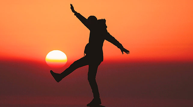 orange sunset photo with a person silhouetted against the sky walking and balancing on a tightrope