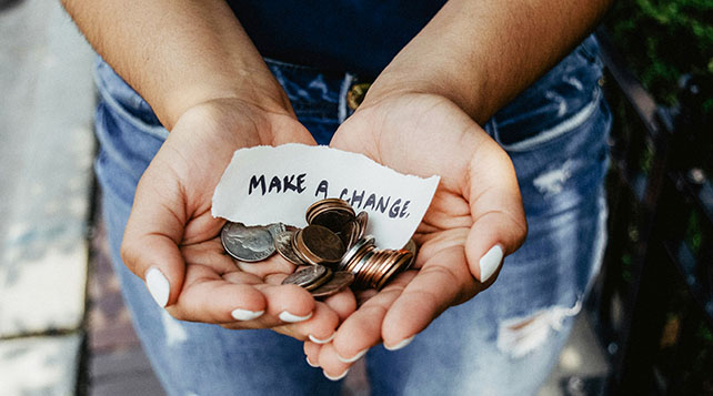 female hands holding an array of coins and a handwritten note that says "Make a Change."