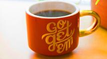 Orange coffee mug with a gold handle. Scripty type on the mug says "go get 'em."
