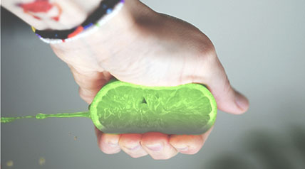 hand with a friendship bracelet squeezing a lime with juice shooting out