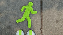 Crosswalk stenciled with a lime green running person stick figure and some white tennis shoes poiting toward it
